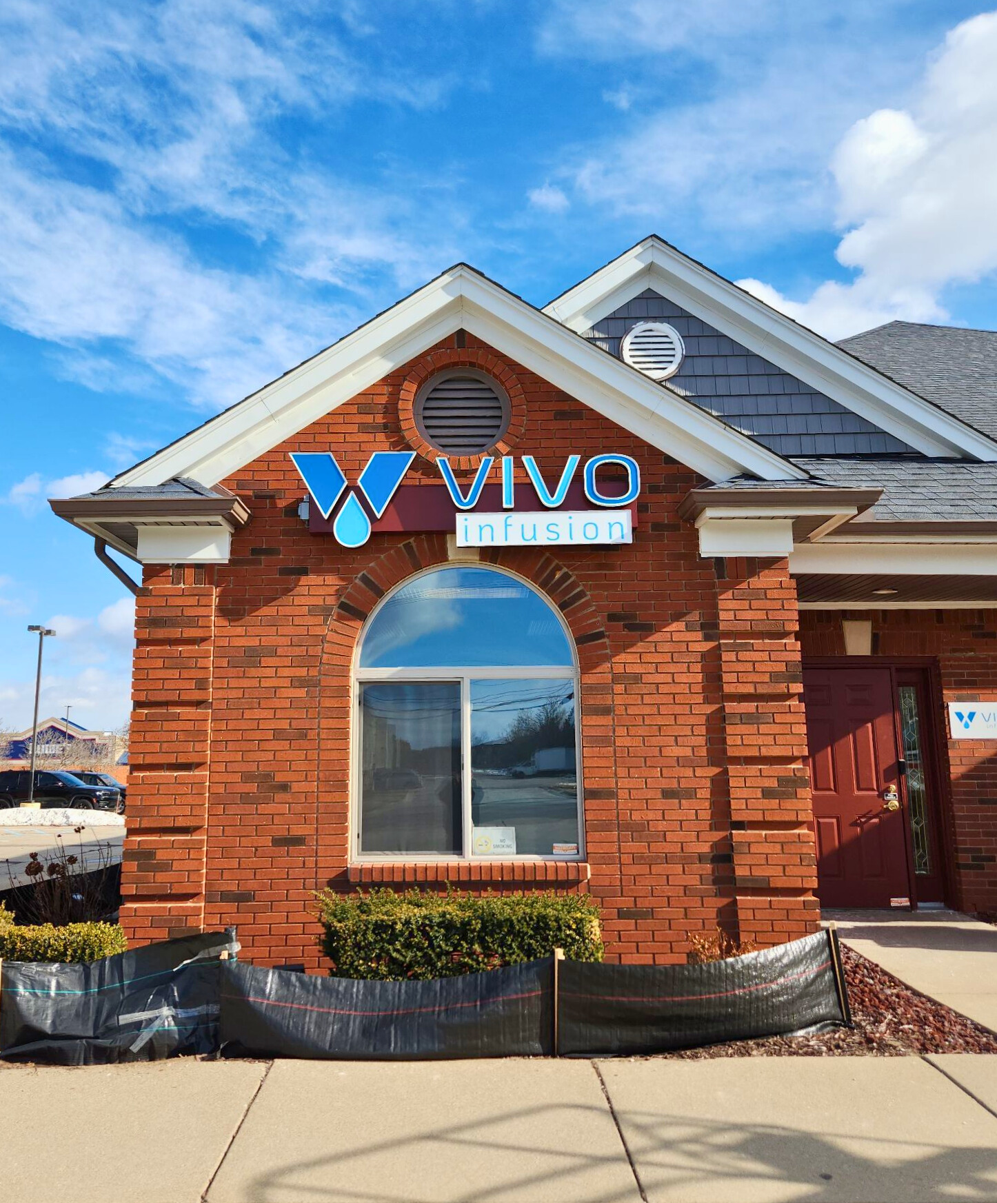 Vivo Infusion Therapy wall sign installed on a red brick medical office building with a blue sky background.