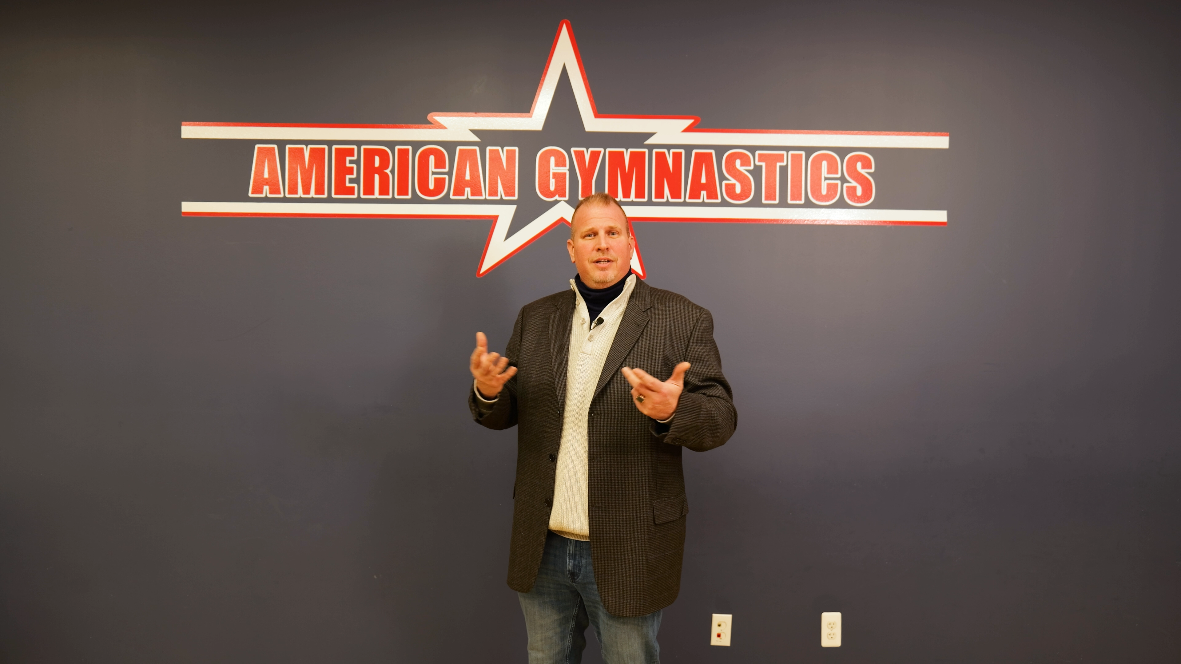 Jeff Miller stands in front of the American Gymnastics logo at the Chesterfield, MI facility.